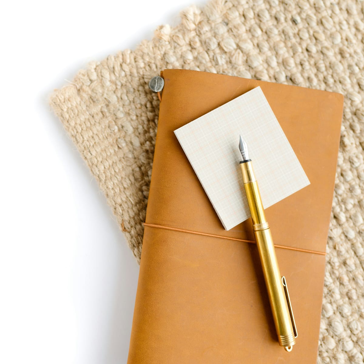A leather journal, a brass pen, and a notepad on a desk.