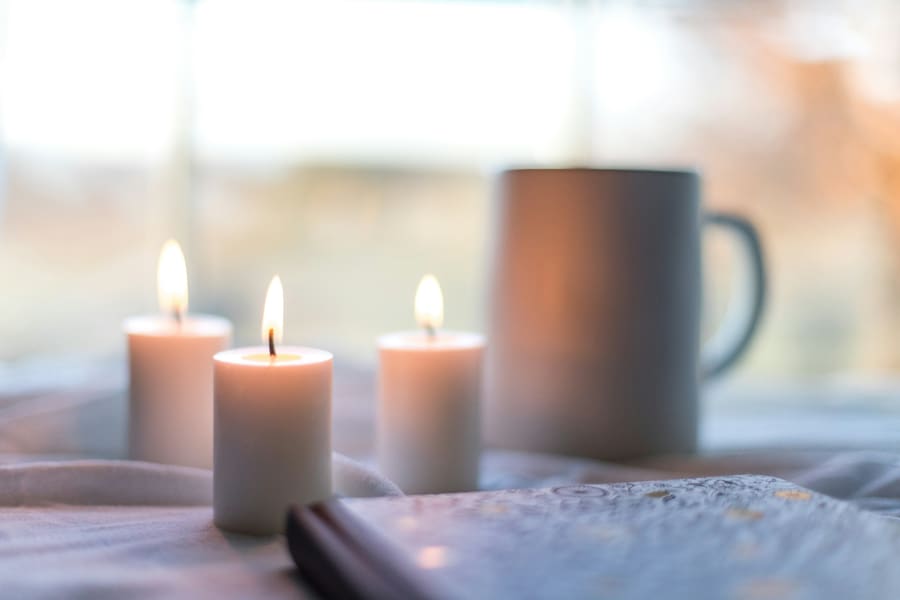 Three lit candles and a mug by a bright window.